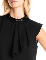 Blusa sin mangas color blanco, confeccionada en crepe con acabado satinado. Presenta un cuello alto decorado con mostacillas y una sobrecapa drapeada en el frente. La espalda cuenta con una abertura tipo gota y cierre de botón.