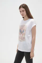 Remera de algodón blanca con estampado frontal de mariposa y texto decorativo en tonos pasteles, de manga corta con dobladillo y calce holgado.