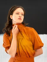 Blusa color ocre de algodón tipo seda, teñida a mano con técnica tie dye. Tiene corte recto, cierre invisible en el escote delantero y mangas regulables con elástico.