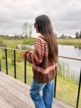 Sweater de punto con diseño jacquard en la parte superior, cuello redondo y mangas largas. Presenta una combinación de colores en tonos tierra, marrón y rosado.