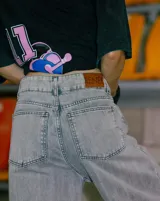 Jean de corte oversize con tiro medio-alto, confeccionado en denim de algodón con lavado tipo ice wash en tono grisáceo. Presenta diseño de cinco bolsillos, cierre frontal y etiqueta de cuero en la parte posterior de la cintura.