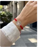 Pulsera de hilo rojo en macramé con dije central circular de plata 925 que presenta el símbolo del tetragramaton calado. Posee terminaciones con esferas de plata y sistema de ajuste regulable.