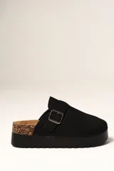 Zueco de plataforma color negro, con capellada de gamuza sintética y detalle de hebilla metálica ajustable en el empeine. Presenta una base de corcho en el talón y suela dentada de goma.