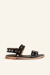 Sandalia baja de cuero vacuno color negro con acabado efecto charol texturizado, decorada con tachas metálicas plateadas en las tiras y la sujección del talón. Cuenta con suela plana de cuero.