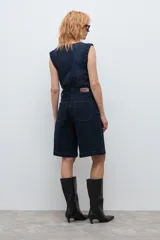 Bermuda de jean en color azul oscuro, con corte recto y largo hasta la rodilla. Presenta costuras a la vista en tono contrastante, cierre frontal con botón y bolsillos laterales.