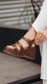 Sandalia de cuero marrón con plataforma corrida y taco alto texturizado. Posee tiras delanteras múltiples y una pulsera al tobillo con hebilla ajustable.