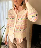 Cárdigan de punto con diseño jacquard floral en tonos rosa, amarillo y verde sobre base color crema. Presenta cuello en V, cierre frontal con botones grandes y detalles de calados en el tejido.