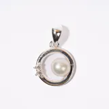 Dije plateado con forma circular, una perla blanca y tres pequeñas piedras brillantes.