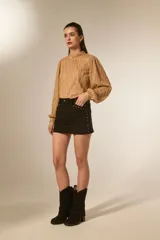 Minifalda negra de poliéster con corte al cuerpo, tiro alto y detalle de tachas doradas decorativas a lo largo de la costura lateral y el bolsillo delantero.