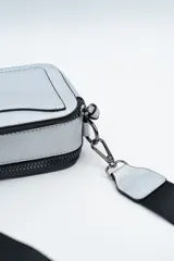 Bandolera de diseño rectangular en color negro, confeccionada en material texturizado. Cuenta con una correa de hombro ajustable y extraíble, cierre superior y tiradores laterales decorativos.