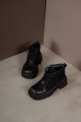 Borcegos de punta cuadrada con diseño acordonado, combinando paneles de cuero texturizado y gamuza en tonos marrones. Presentan una suela track gruesa de goma negra y cordones negros.