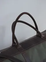 Bolso de lona color verde militar con detalles en cuero marrón. Tiene doble asa de mano y correa de hombro ajustable y extraíble.