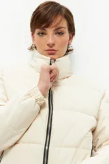 Campera puffer corta color beige de nylon, con cuello alto, cierre frontal y bolsillos laterales con cierre.