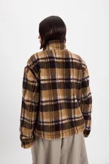 Campera de corderito sintético con diseño a cuadros en tonos marrones y negros. Presenta cuello alto, cierre frontal completo y detalles de paneles en color marrón liso. El diseño es de silueta holgada, largo tipo crop y cuenta con un cordón elástico ajustable en el ruedo.