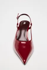 Zapato de tacón destalonado con acabado efecto acharolado, diseño de punta fina y cierre mediante tira trasera con hebilla metálica ajustable.