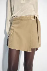 Falda pantalón cruzada de tiro medio en color tostado, con diseño estilo cargo que incluye bolsillos de parche con solapa y detalle de argolla metálica. Cuenta con trabillas y un cinturón integrado con hebilla metálica.