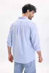 Camisa de lino de manga larga con diseño a rayas en color azul claro y blanco, cuello abotonado y cierre frontal de botones.