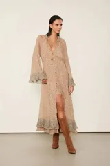 Vestido largo beige estampado con diseño floral, con forro, escote en V con cierre de botones delanteros y mangas largas con puños anchos con volados. Presenta una silueta fluida, detalles plisados y un volante superpuesto en el bajo.
