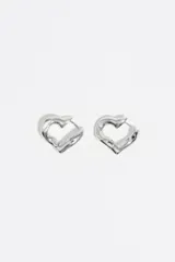 Caravanas de aro con forma de corazón y acabado metálico plateado. Presentan un diseño de líneas fluidas y cierre de gancho. Fabricadas en latón.