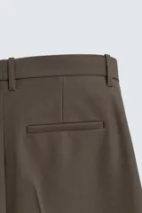 Bermuda de vestir color marrón oscuro, corte relajado y tiro alto, con pliegues frontales y cierre de botón y cremallera.