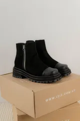 Bota corta de gamuza marrón con puntera de cuero liso, suela track negra y correa desmontable con tachas metálicas.