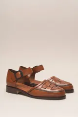 Zapato de cuero color borgoña, con puntera redondeada y diseño trenzado. Presenta una tira sobre el empeine con hebilla metálica negra.