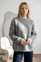 Sweater de punto gris con textura suave, diseño oversize, cuello redondo y detalles de costuras expuestas en color blanco en mangas y ruedo.