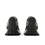 Championes New Balance modelo 327 para mujer, en tonos de gris oscuro y negro. Presentan una combinación de materiales como ante y malla, con el logo 'N' grande y asimétrico en textura de gamuza. La suela es de cuña ensanchada con relieve inspirado en zapatillas de trail.