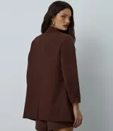 Blazer de sastrería color bordó, de corte oversized y largo, confeccionado en crepé. Presenta solapas clásicas, bolsillos frontales y detalle de pliegues en los puños.