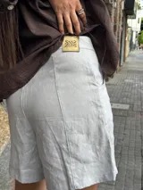 Short de lino en color celeste, con diseño de tiro alto, cierre frontal con botón a la vista y costuras decorativas verticales en el frente.