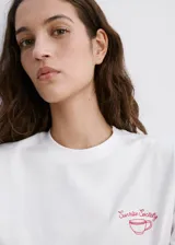 Remera blanca de manga corta y cuello redondo, confeccionada en algodón 100%. Presenta un pequeño bordado en el pecho.