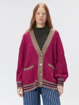Cardigan de tejido de punto con diseño de ochos, corte oversize y mangas largas con puños acanalados. Presenta un escote en V con solapas en contraste, cierre frontal con botones y dos bolsillos delanteros con bordes en contraste. El diseño incluye detalles de rayas en los puños y en el ruedo.
