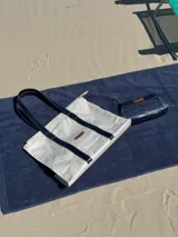 Necessaire de diseño rectangular, confeccionado en una combinación de cuero azul marino y material vinílico transparente. Cuenta con cierre superior, correa de muñeca desmontable y una etiqueta de cuero con el logo de la marca grabado en el frente.