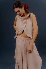 Chaleco de lino color marfil o beige claro, con diseño sin mangas, cuello alto amplio, cierre frontal con botones y bolsillos delanteros amplios. Presenta un corte asimétrico y relajado.