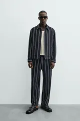 Sobrecamisa de hombre, corte relajado, color azul marino con rayas verticales blancas. Presenta cuello solapa, manga larga con puños abotonados, bolsillos de parche delanteros y cierre frontal de botones.