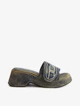 Sandalias de plataforma estilo mule, confeccionadas en denim de algodón lavado azul. Cuentan con una tira ancha ajustable con velcro que lleva el logotipo ovalado de Diesel en relieve. La suela es de plataforma gruesa con tacón curvo y banda de goma dentada.