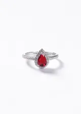 Anillo de plata 925 con piedra central roja en forma de gota rodeada por un halo de zirconias pequeñas y banda decorada con zirconias laterales.