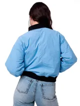 Campera tipo bomber de color azul claro, con cierre frontal, puños y cintura acanalados en color negro. Presenta un bolsillo pequeño con cierre en el pecho y el logo de la marca Caterpillar en una etiqueta rectangular. Cuenta con forro interior acolchado y diseño corto.