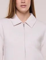 Camperita corta blanca de punto elastizado, con cuello camisero, cierre frontal completo y mangas largas con puños anchos abotonados.