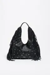 Bolso de hombro tipo hobo de piel vacuna negra, con estructura blanda, adornado con tachas metálicas circulares plateadas y flecos largos en los laterales. Presenta un asa de hombro y el logo de Bimba y Lola grabado en la parte inferior central.