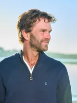 Sweater de tejido de punto fino en color azul marino, con diseño de medio cierre frontal y cuello alto. Presenta puños y ruedo acanalados, con un pequeño bordado distintivo en el pecho.