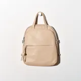 Mochila pequeña color beige, con doble asa de mano y tiras traseras regulables. Presenta un bolsillo frontal con cierre y un adorno colgante de madera.