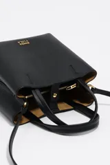 Bolso pequeño de piel color borgoña, con estructura rígida y forma de cubo. Posee doble asa de mano y una correa larga para llevar al hombro o cruzado. El frente lleva el logo metálico de Bimba y Lola.