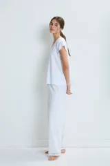 Pijama de dos piezas en color blanco, confeccionado en algodón. Incluye una remera de manga corta con cuello en V y detalles de calados, y un pantalón de corte recto con detalles de calados en el ruedo.