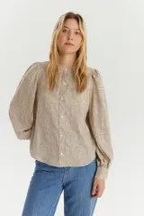 Blusa de manga larga con diseño de hombros abullonados y cuello redondo pequeño. Presenta cierre frontal con botones y un estampado fino de puntos sobre fondo beige.