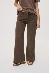 Pantalón jean de tiro medio, color negro, de corte amplio y silueta extra wide leg. Presenta diseño clásico de cinco bolsillos, cierre frontal con botón y cremallera, y detalle de tachas metálicas aplicadas a lo largo de los laterales.
