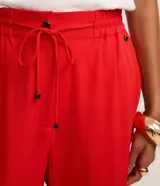 Pantalón de crepé rojo, modelo estilo pijama, de corte fluido, con cintura elástica y lazo de ajuste con terminales metálicas. Cuenta con bolsillos laterales y cierre frontal con cremallera y botón.