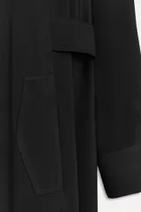Vestido camisero largo negro con cuello solapa, manga larga con puños, bolsillos delanteros y cinturón ajustable con trabillas y botones. Cierre frontal con botones.
