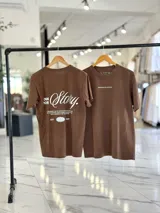 Remera oversize de manga corta color marrón con efecto gastado. Presenta inscripciones estampadas en color blanco en el frente y en la espalda.