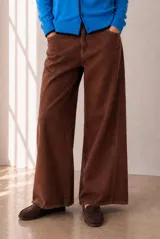 Jeans de corte ancho color marrón, de tiro medio con bolsillos delanteros y traseros, y botamanga con flecos.